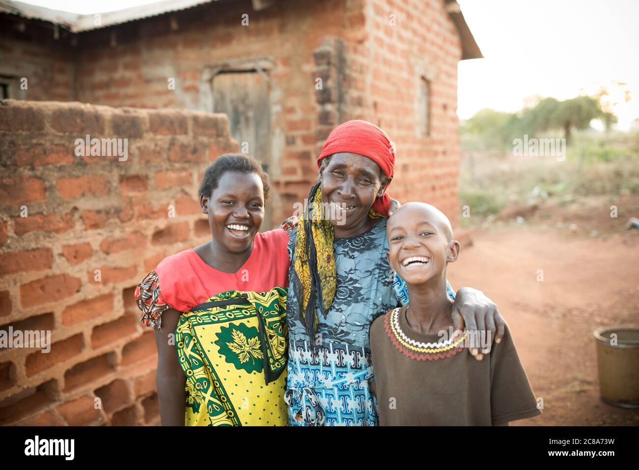 Regina Mwangangi (65), her daughter-in-law Mary Muinde (20), and granddaughter Teresia Monica (11), stand outside their home in Makueni County, Kenya. Stock Photo