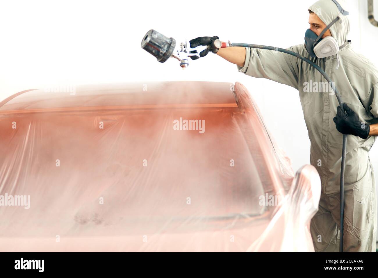 Man with protective clothes and mask painting car roof using compressor