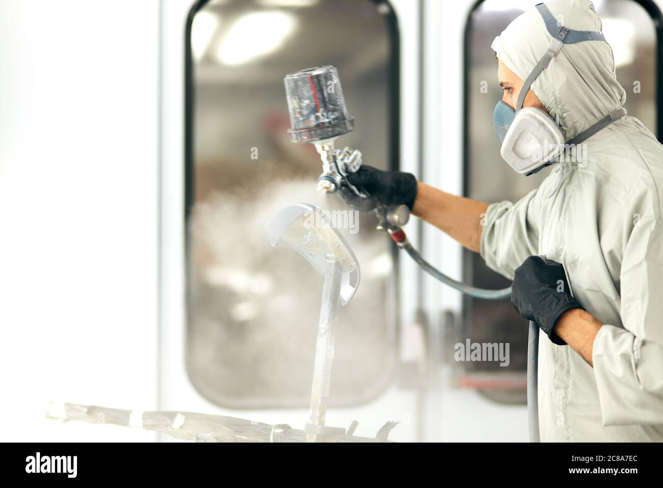 Man with protective clothes and mask painting car roof using compressor