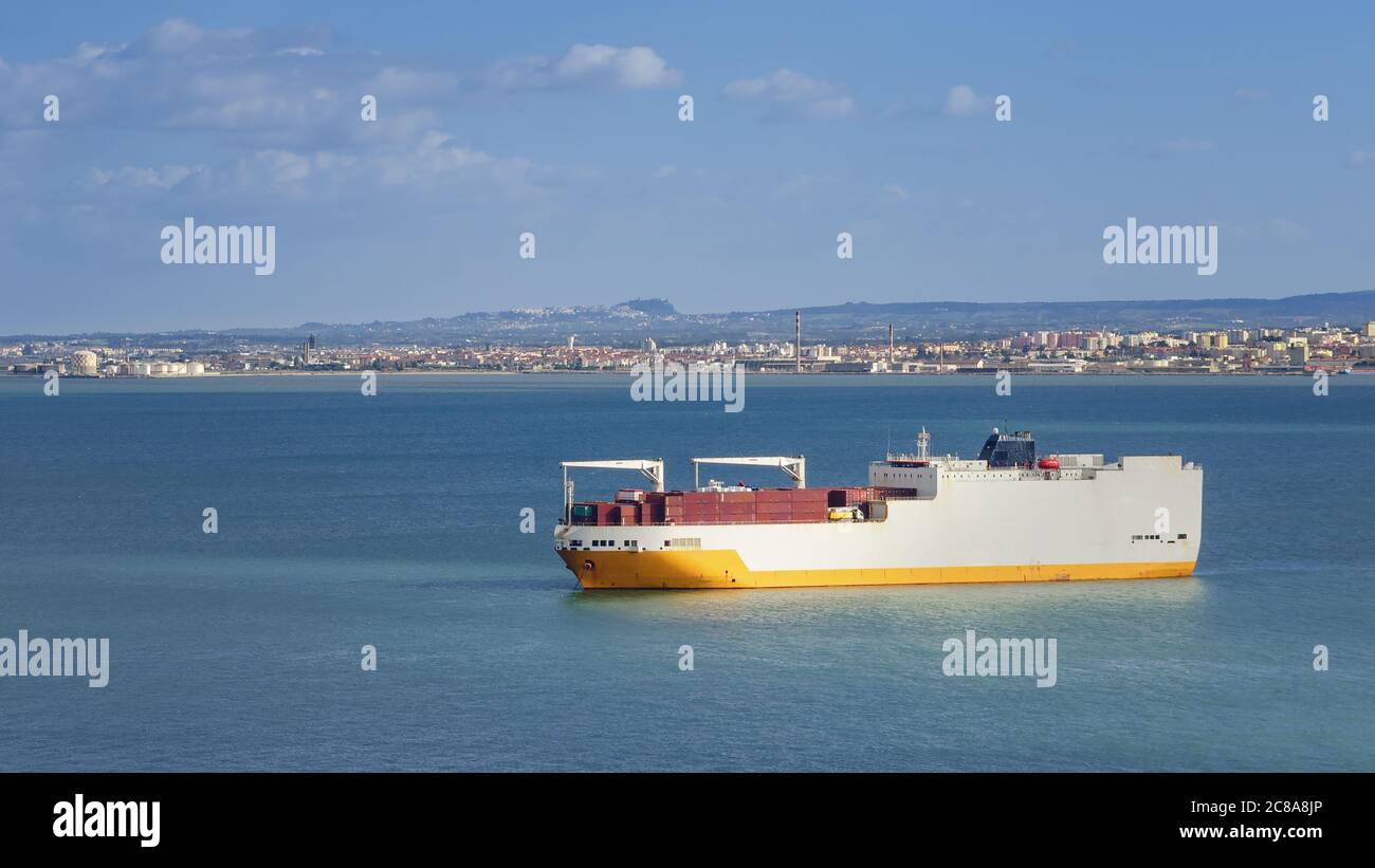 white and yellow geared container ship sailing from lisbon port along the estuary of river tagus to the atlantic ocean Stock Photo