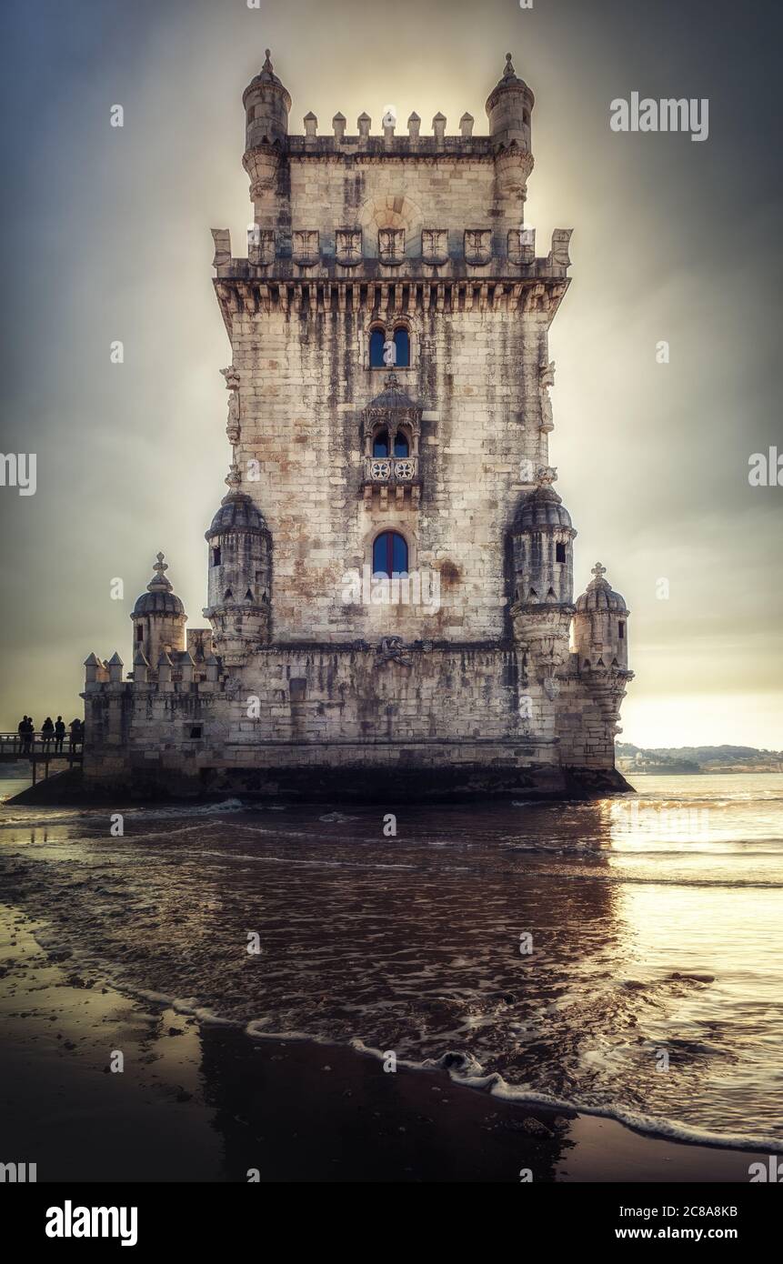 dramatic sunset and waves on the shore of the tagus river near the Tower of Belem, ancient bastion, fortress and symbol of Lisbon and of portuguese ag Stock Photo