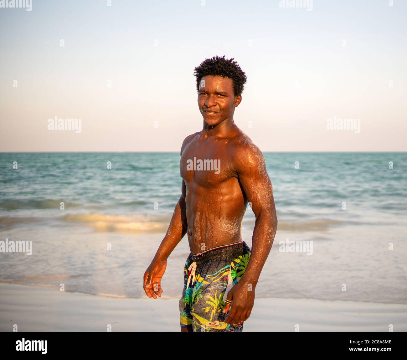 Young Attractive Muscular and Strong Athletic Black African Man Smiling at the White Sand Beach Stock Photo