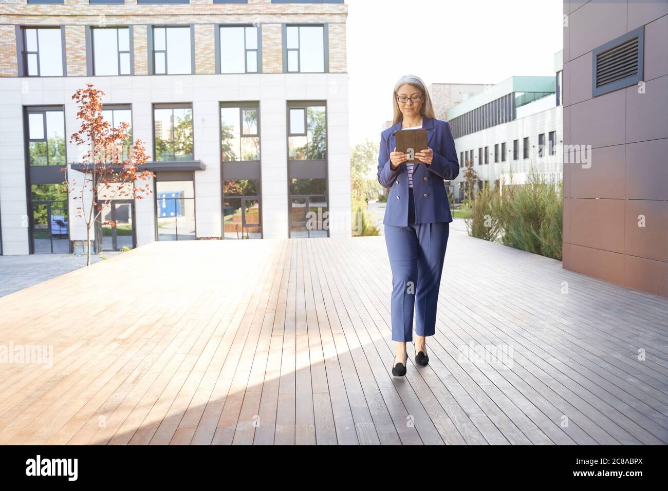 Working online. Portrait of a confident mature business woman in classic suit using digital tablet standing against office building outdoors. Checking email. Business people and modern technologies Stock Photo