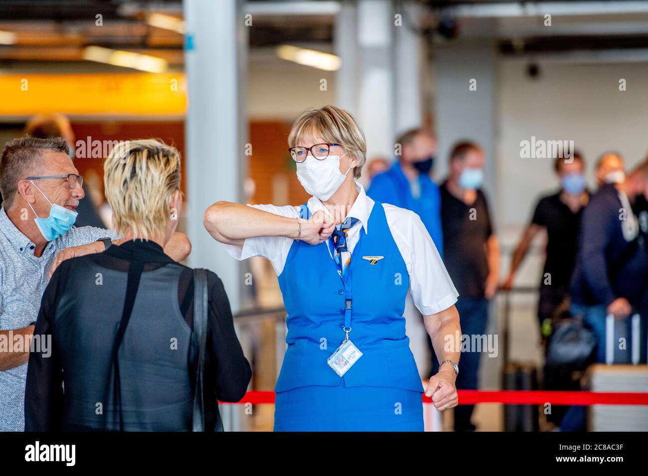 A KLM staff doing the elbow bump with travellers while wearing a face mask as a precaution against the spread of the covid 19 virus at the airport.Summer holiday travellers making it busy again at Schiphol airport as KLM airline receives a support package of 3.4 billion euros to take it through the coronavirus crisis. Stock Photo