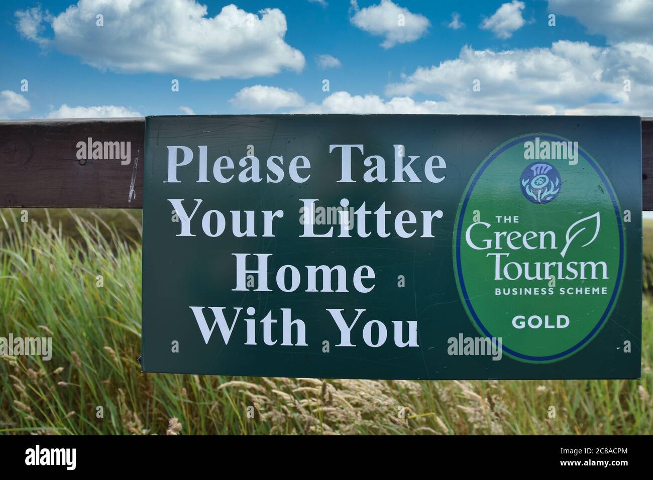 Please take your litter home with you sign in Scotland. Summertime. Wooden fence, green field, blue sky and clouds background. Stock Photo