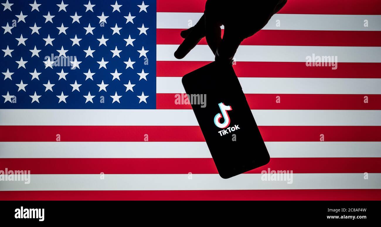 Stone / United Kingdom - July 22 2020: TikTok  logo seen on the silhouette of smartphone hold in a hand with blurred American flag on tha back. Rela p Stock Photo