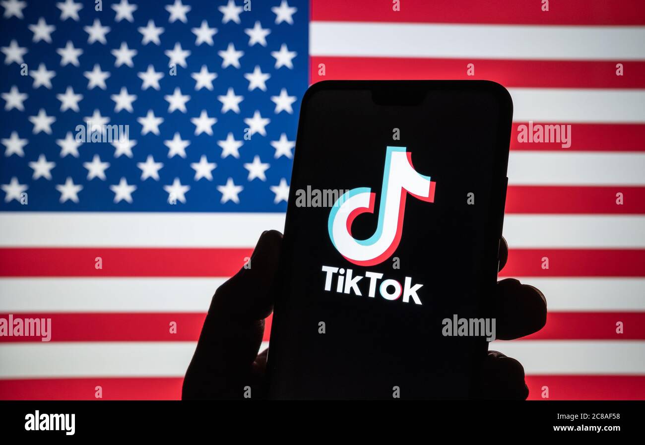 Stone / United Kingdom - July 22 2020: TikTok  logo seen on the silhouette of smartphone hold in a hand with blurred American flag on tha back. Rela p Stock Photo