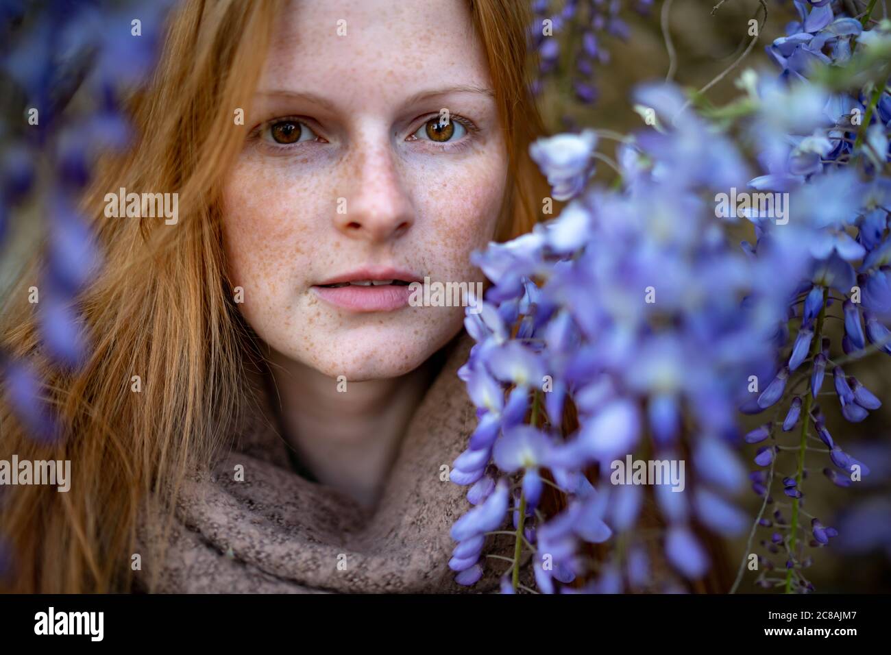 Close-up portrait of woman with freckles by blue flowers Stock Photo