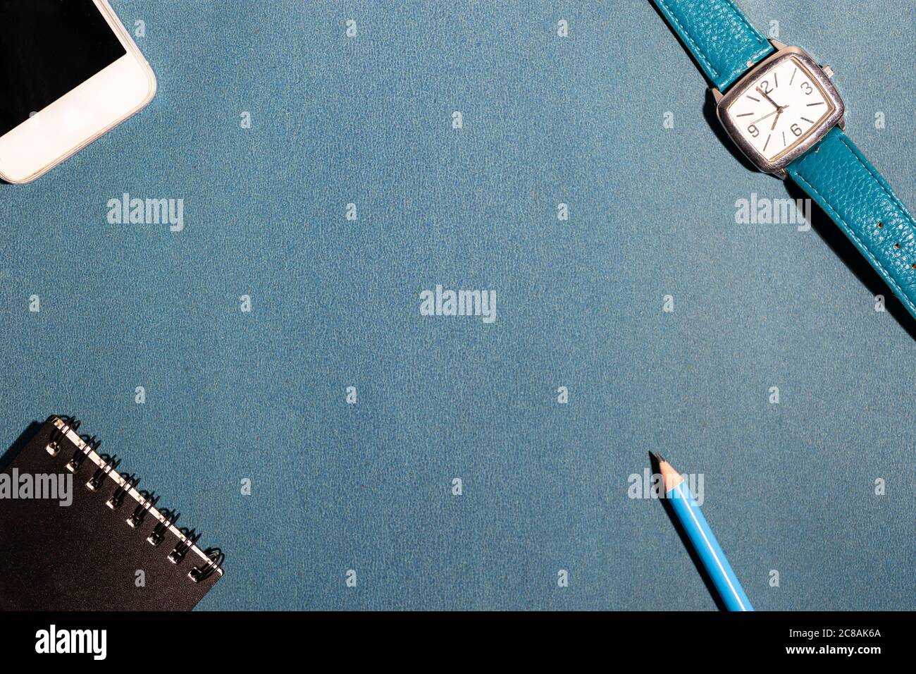 Pencil, smartphone, watch and a small notebook on the four corners of a  blue surface Stock Photo