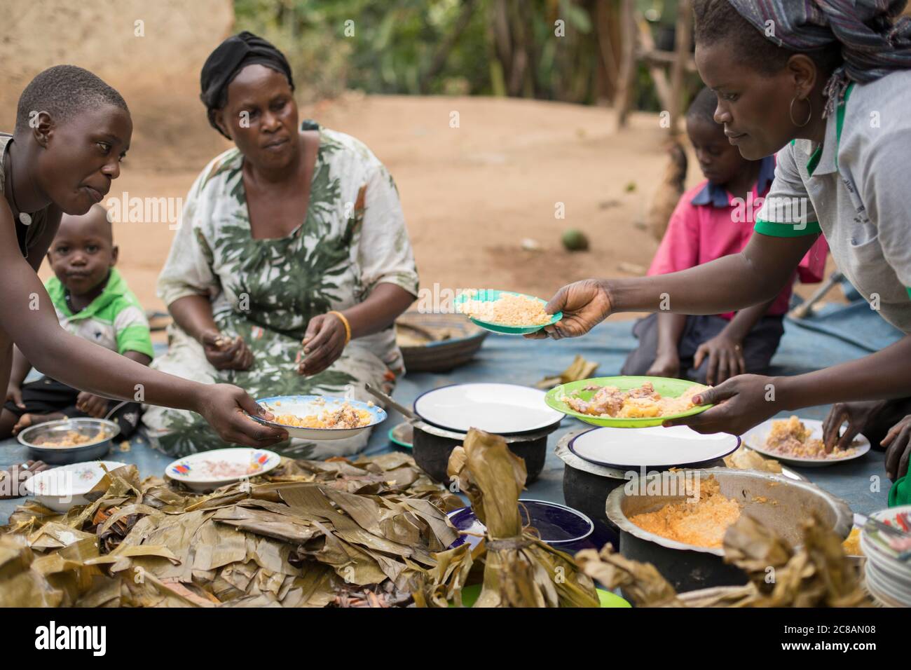 A family is seated outside their house to share a meal together in Kyotera District, Uganda, East Africa. Stock Photo