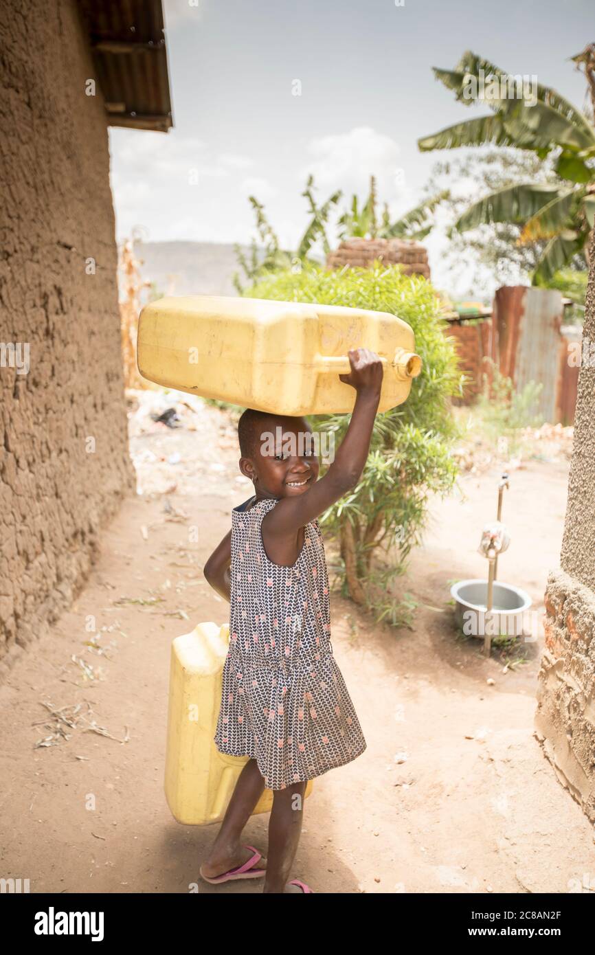 A happy young child fetches water, carrying jerrycans on her head, in Rakai District, Uganda, East Africa. Stock Photo