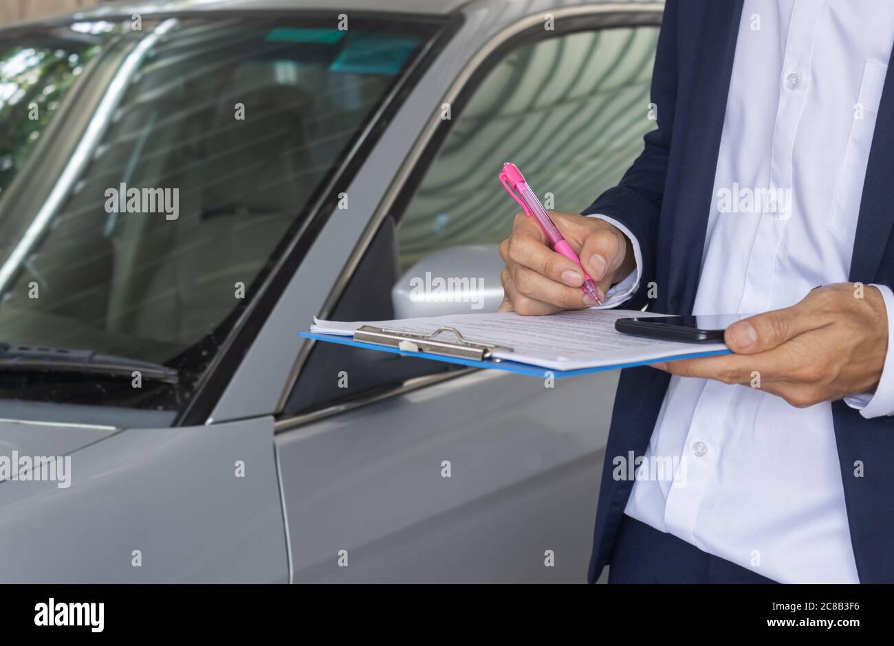 Standing Asian Insurance Agent or Insurance Agency in Suit Checking Car Crash Data Report from Accident for Claim at Outdoor Place Stock Photo