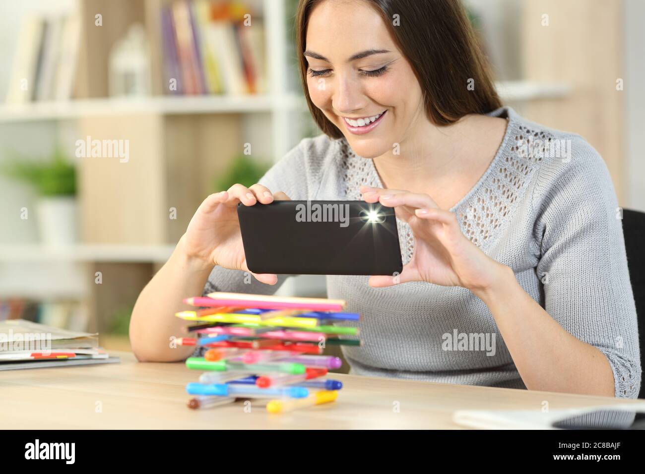 Happy woman taking photo with flash on smart phone sitting on a desk at home Stock Photo