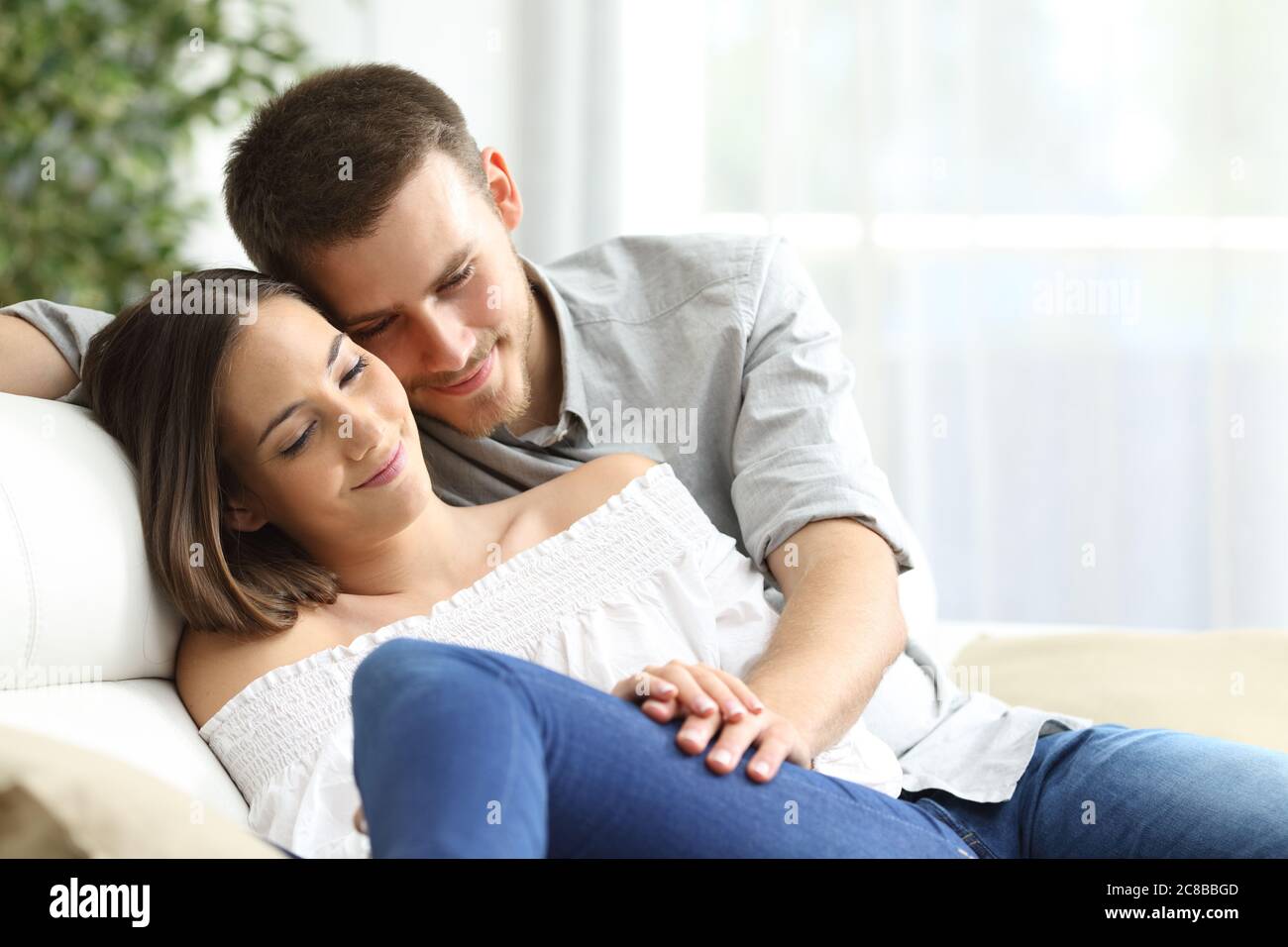 Happy couple in love cuddling holding hands sitting in the sofa in the living room at home Stock