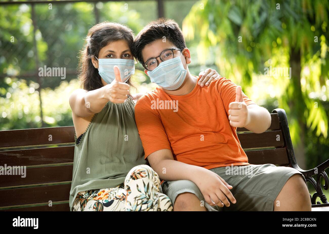 Mother and son with protective face mask giving thumbs up at park Stock Photo