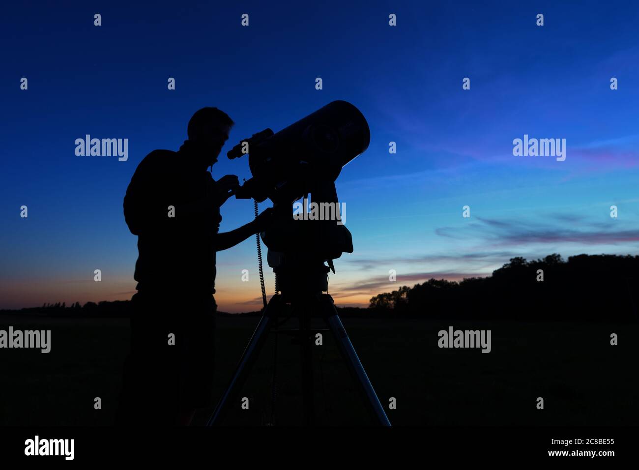 silhouette of a man setting up a telescope for night observation on dark blue sky at dusk Stock Photo