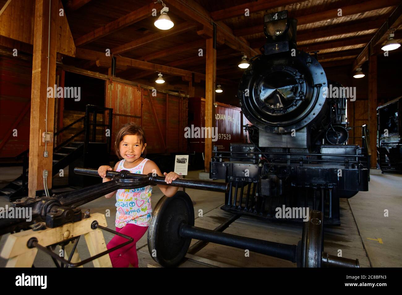Young girl posing in front of an old steam train in a train shed. Stock Photo