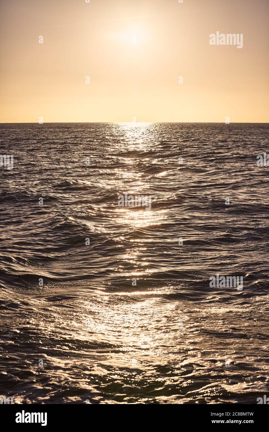 Sunset over the sea reflected in water, focus on waves in the middle of the scene. Stock Photo