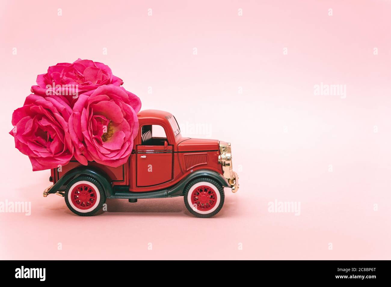 Red toy truck delivering bouquet of rose flowers on pink background. February 14, Valentine's day, 8 March, International Women's Day. Flower delivery Stock Photo