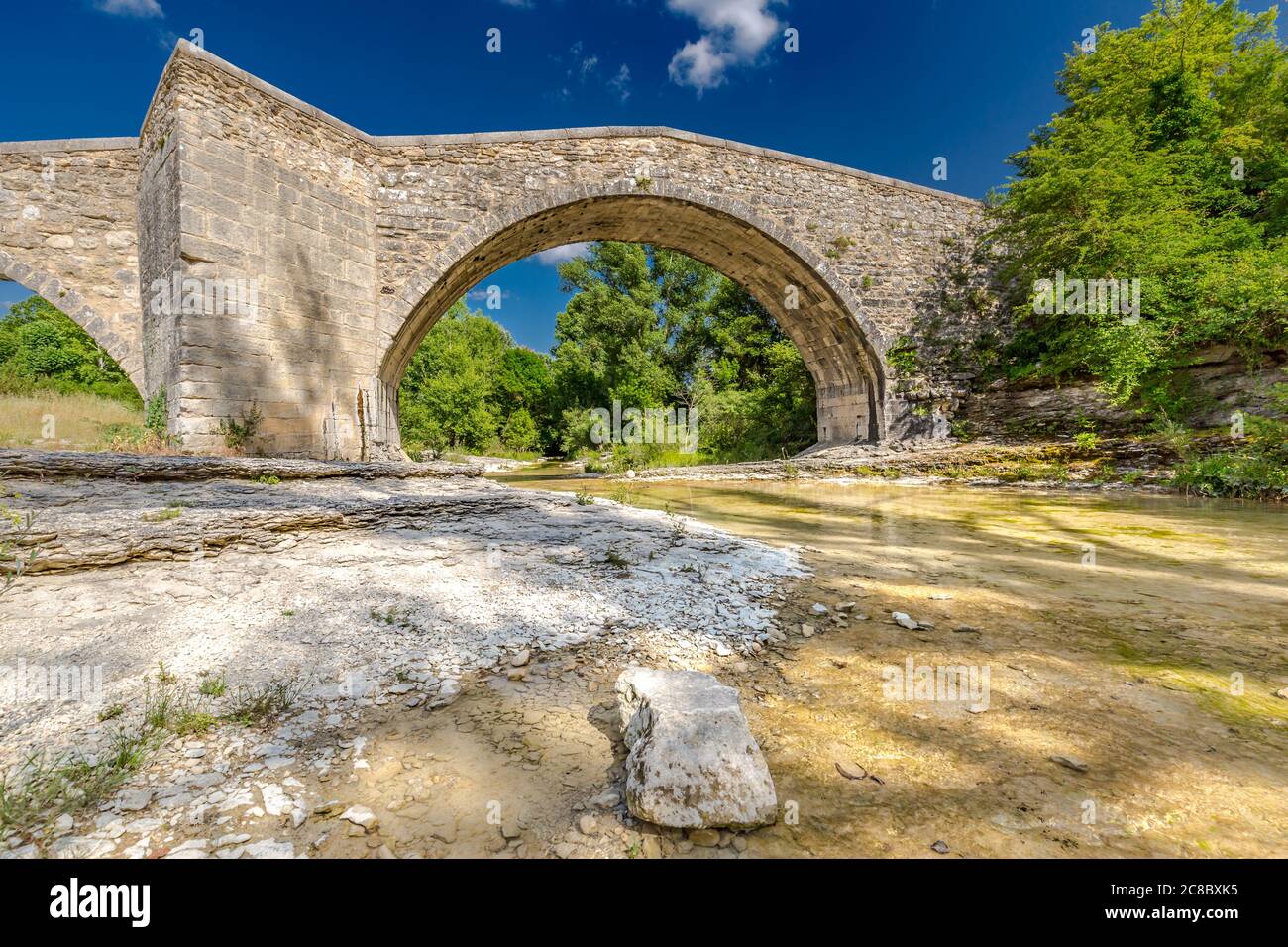 Romanesque Bridge of Mane. Old stone bridge in summer with green trees and blue sky. Idyllic historic architecture Stock Photo