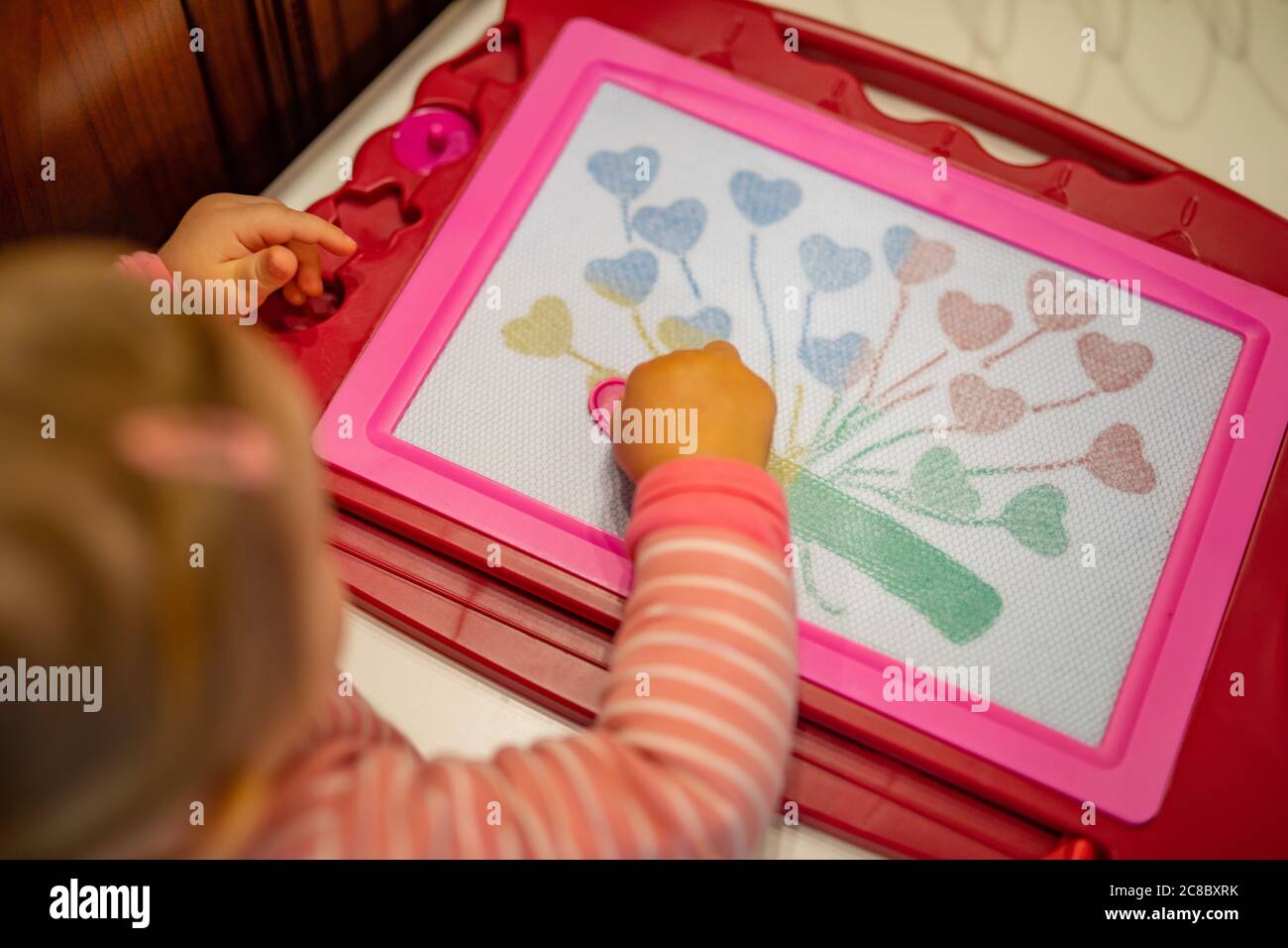 Cute little toddler girl drawing closeup. Magnet board or magic board drawing hearts, cute hands Stock Photo
