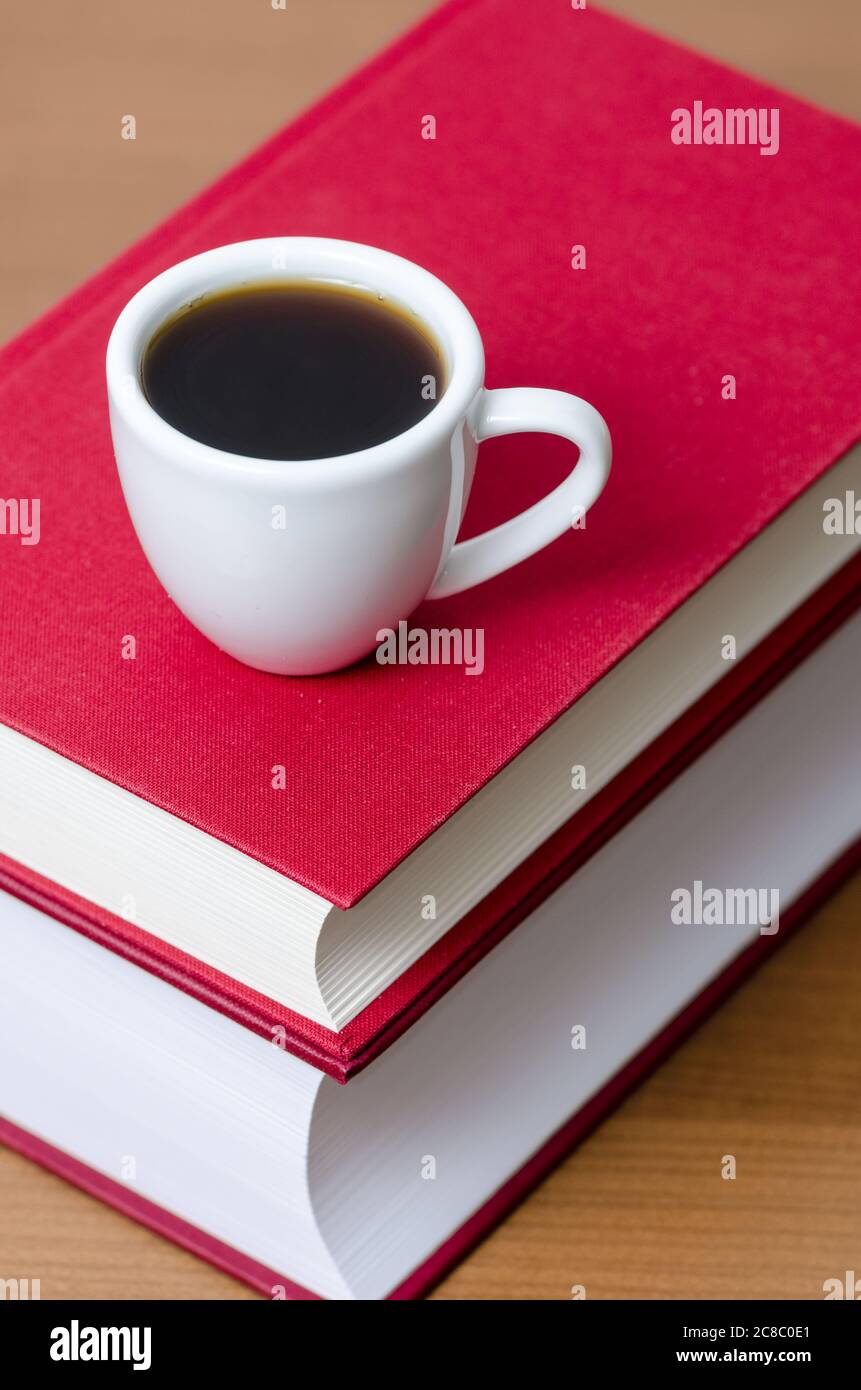 Red hardcover books and white coffee cup or mug with hot beverage on wooden table or desk, indoors, literature, library Stock Photo