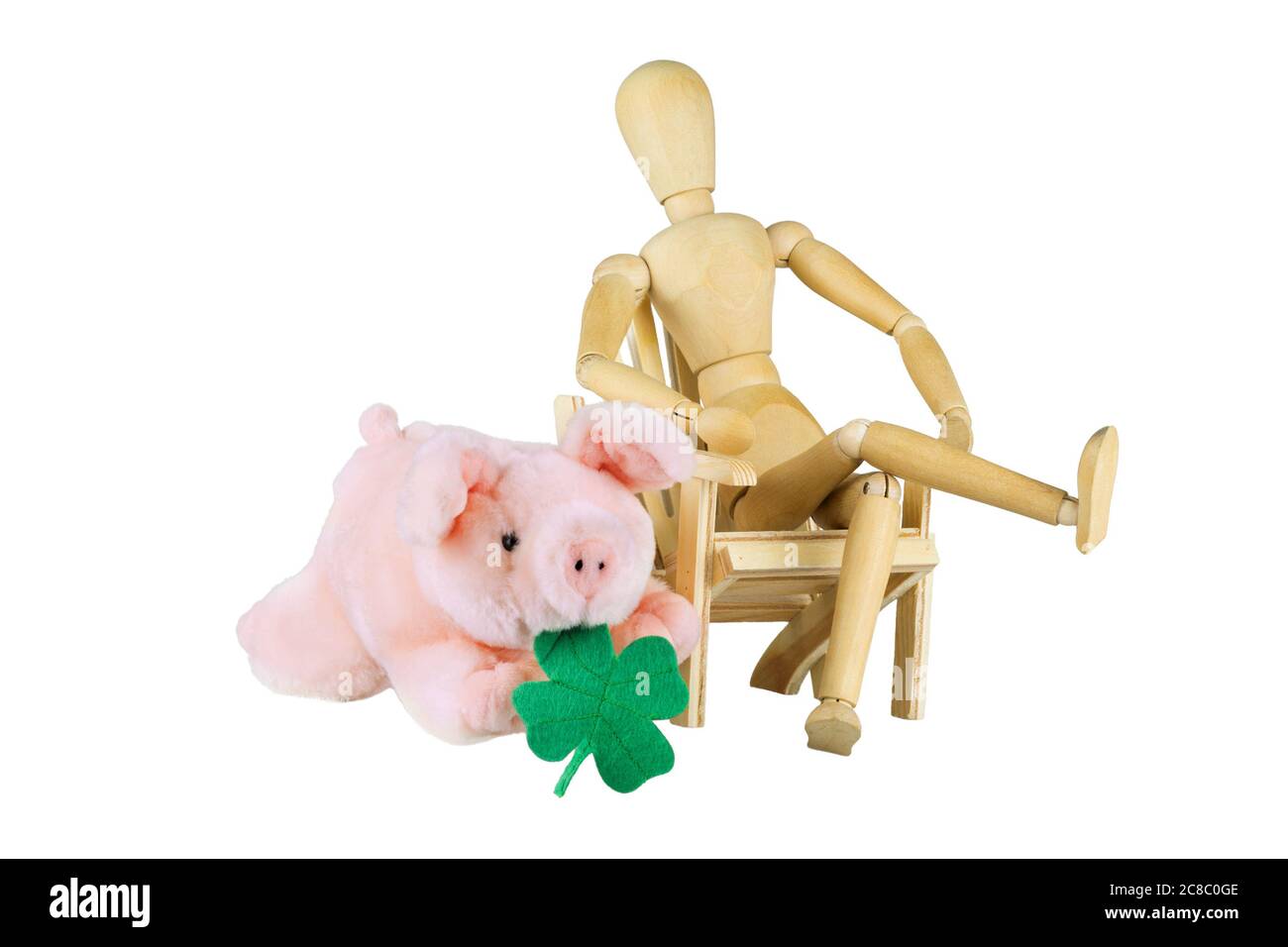 A wooden doll is sitting on a chair next to a plush piggy with shamrock over white Stock Photo