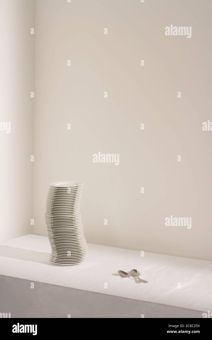 Spoons next to stack of plates on table Stock Photo