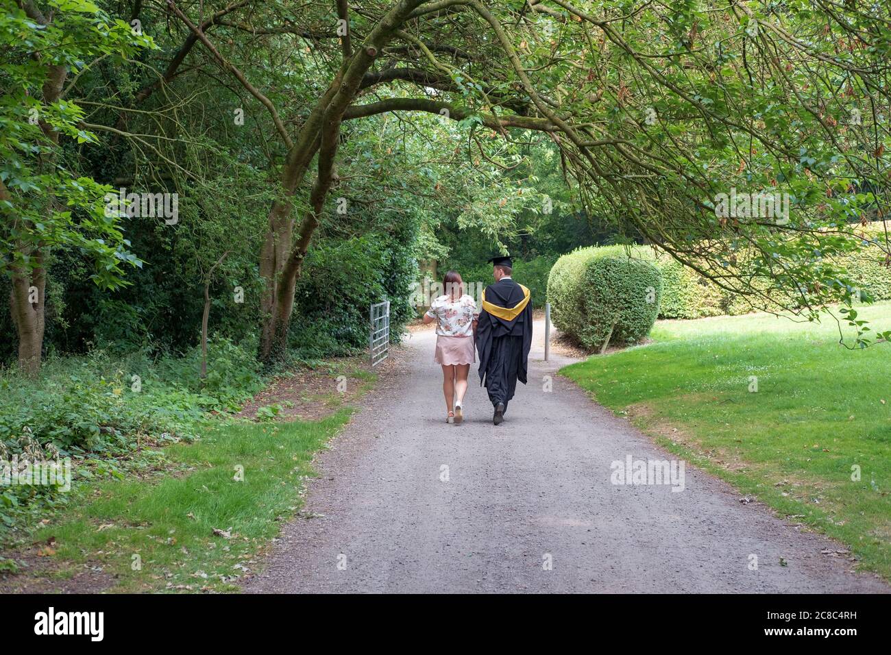 Young couple seen walking in the grounds of a famous UK university. The man is seen wearing his graduation gown and mortar board/ Stock Photo