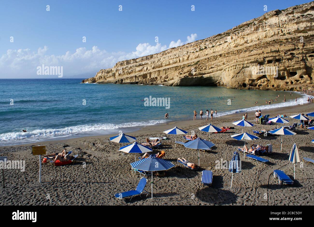 Matala, Crete / Greece / October 15 2010 : Holiday makers relax in the autumn sun at the beach at the charming village of Matala, Crete.  Beautiful ro Stock Photo