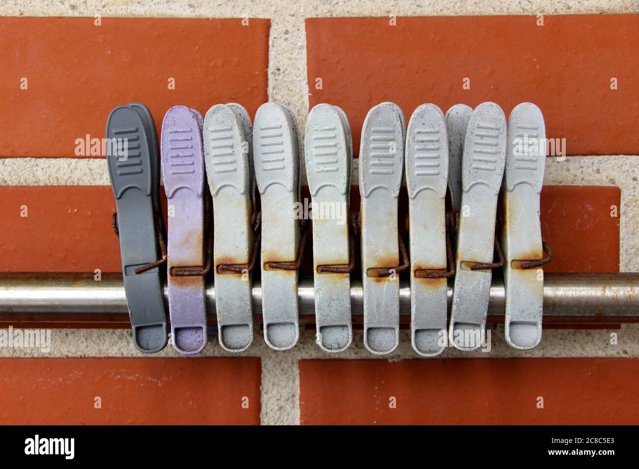 Photo of Old grey and purple plastic pegs with rusting metal on an aluminium rod against a red brick wall Stock Photo
