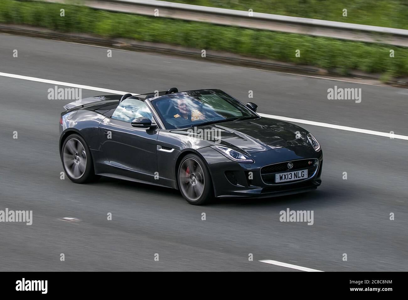 A 2013 Jaguar F-Type S V8 Auto Grey Car Roadster Petrol convertible cabriolet roof down driving on the M6motorway near Preston in Lancashire, UK Stock Photo