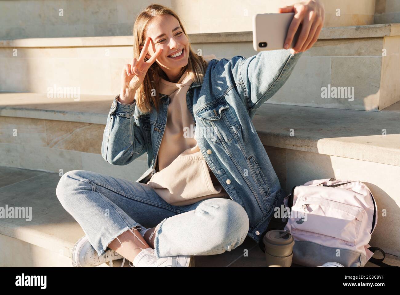 Cheerful young blonde girl taking a selfie with mobile phone while ...