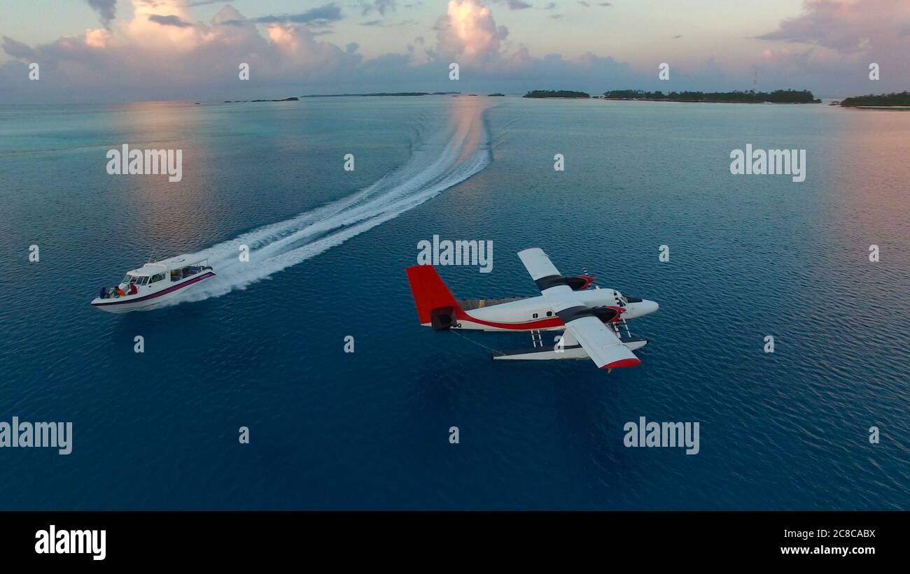 Seaplane during sunset aerial photography. White black red seaplane docked in the middle of the Indian Ocean, Speed boat is passing by Stock Photo