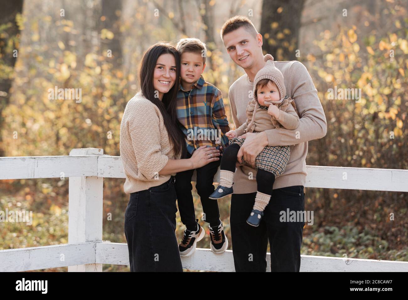 young dad and mom with baby girl and little son walking in autumn ...