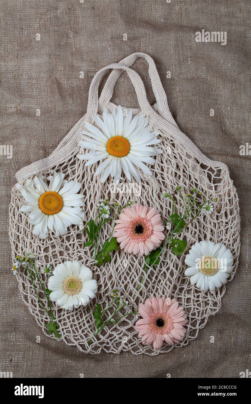 Eco-friendly reusable white cotton mesh bag with fresh flowers on brown background Stock Photo