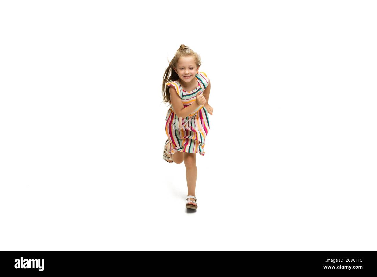 Happy child, little and emotional caucasian girl jumping and running isolated on white background. Looks happy, cheerful, sincere. Copyspace for ad. Childhood, education, happiness concept. Stock Photo