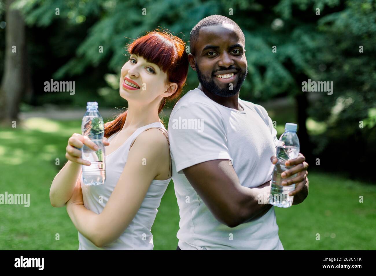 Sport, fitness and family concept. Close up of cheerful smiling multiethnical couple with bottles of water, posing to camera during their break after Stock Photo