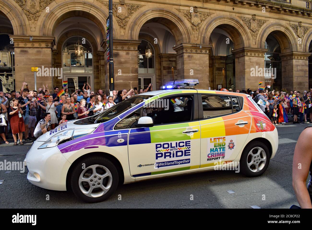 Pride parade passing in front of Radisson Hotel Manchester UK. Police car bearing Police with Pride hate crime logo and Manchester bee symbol Stock Photo
