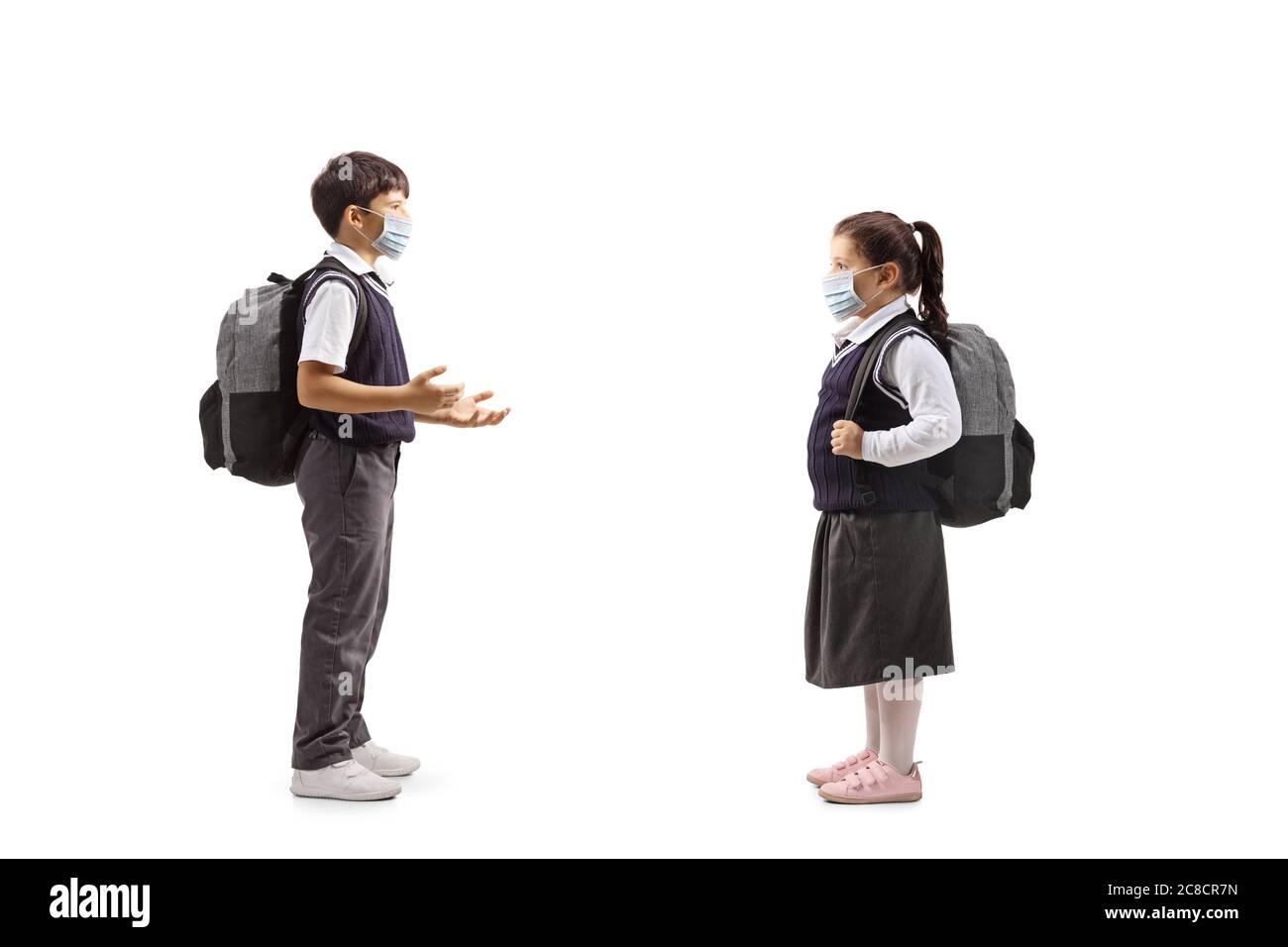 Full length profile shot of a schoolboy talking to a schoolgirl with protective face masks isolated on white background Stock Photo