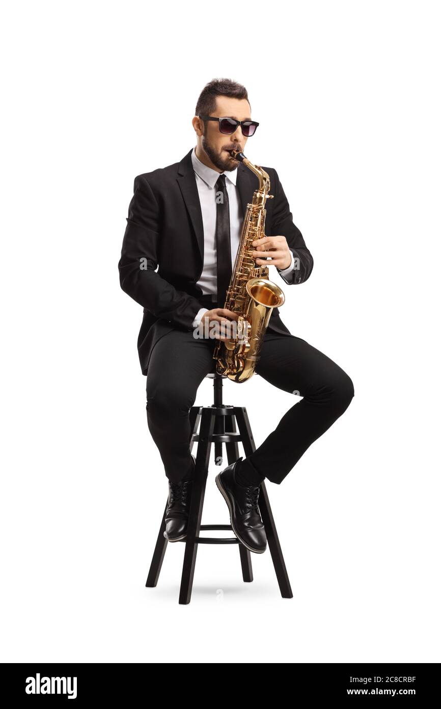 Handsome man in a black suit playing a saxophone and sitting on a chair isolated on white background Stock Photo