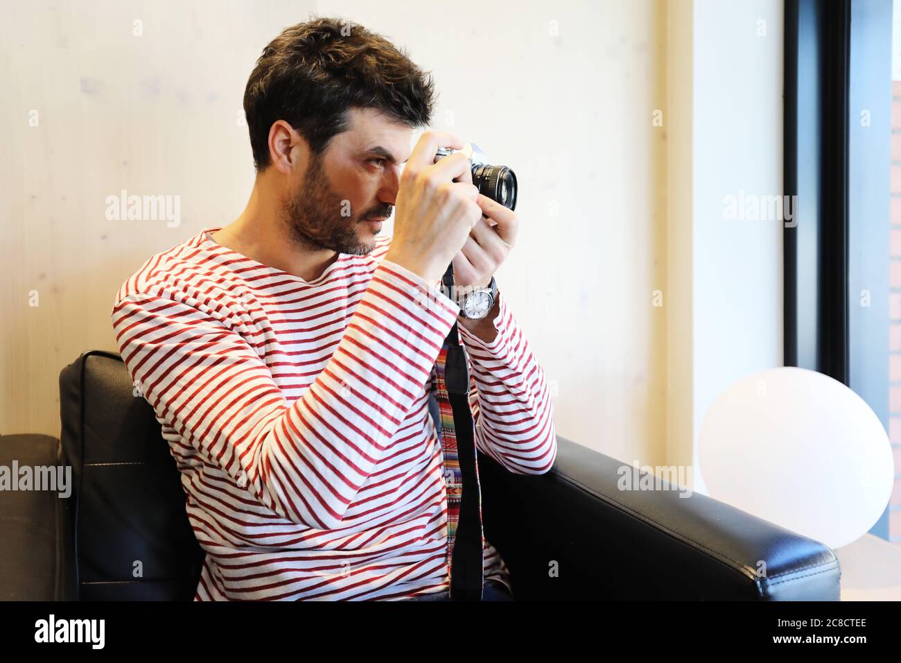 Bearded traveler male sitting on armchair while using a camera Stock Photo