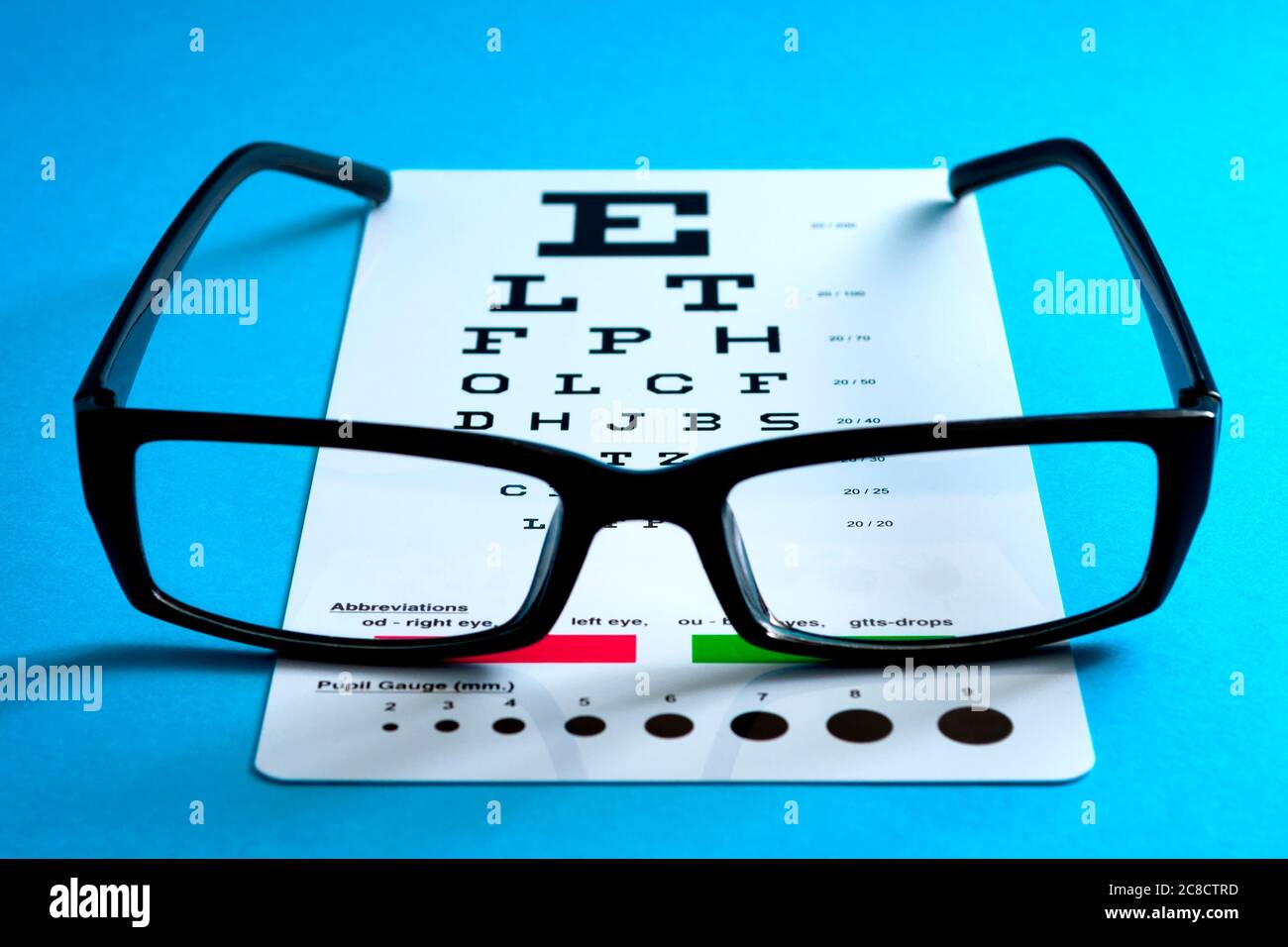 Ophthalmological exam, healthy eyes and ophthalmology concept with a pair of vision glasses and an eye chart isolated on blue background Stock Photo