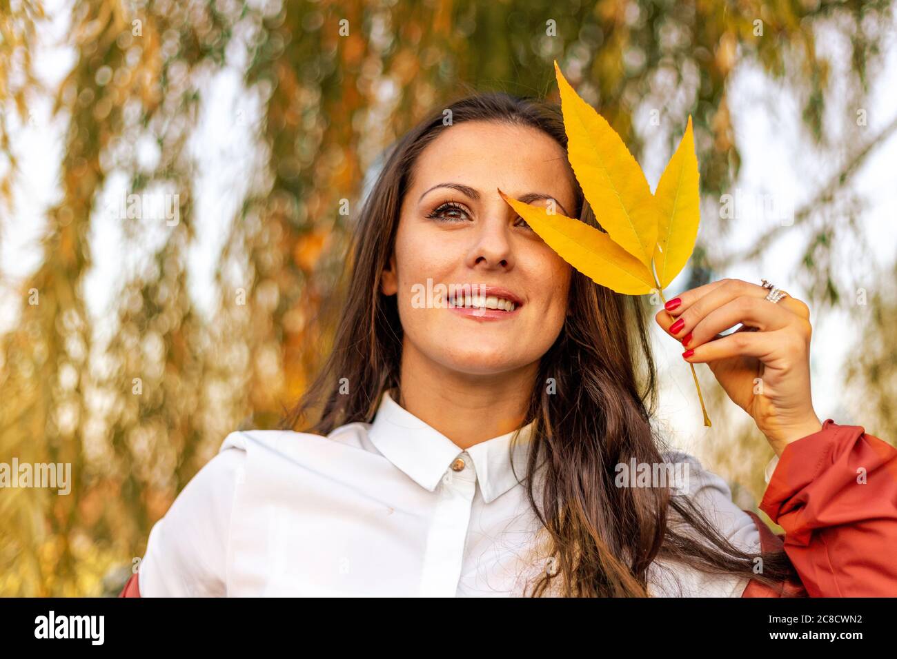 Beautiful young woman holding leaf in front of her face. Autumn vibes ...