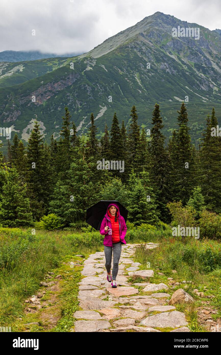 Woman with the umbrella walking up the tourist trail in the rain in Tatra mountains in Poland Stock Photo
