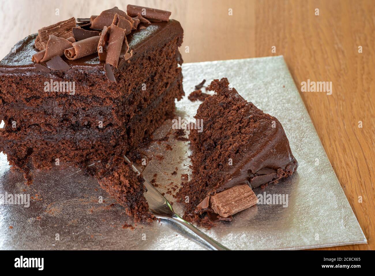 Half eaten chocolate cake, with fork and silver cake board. Stock Photo