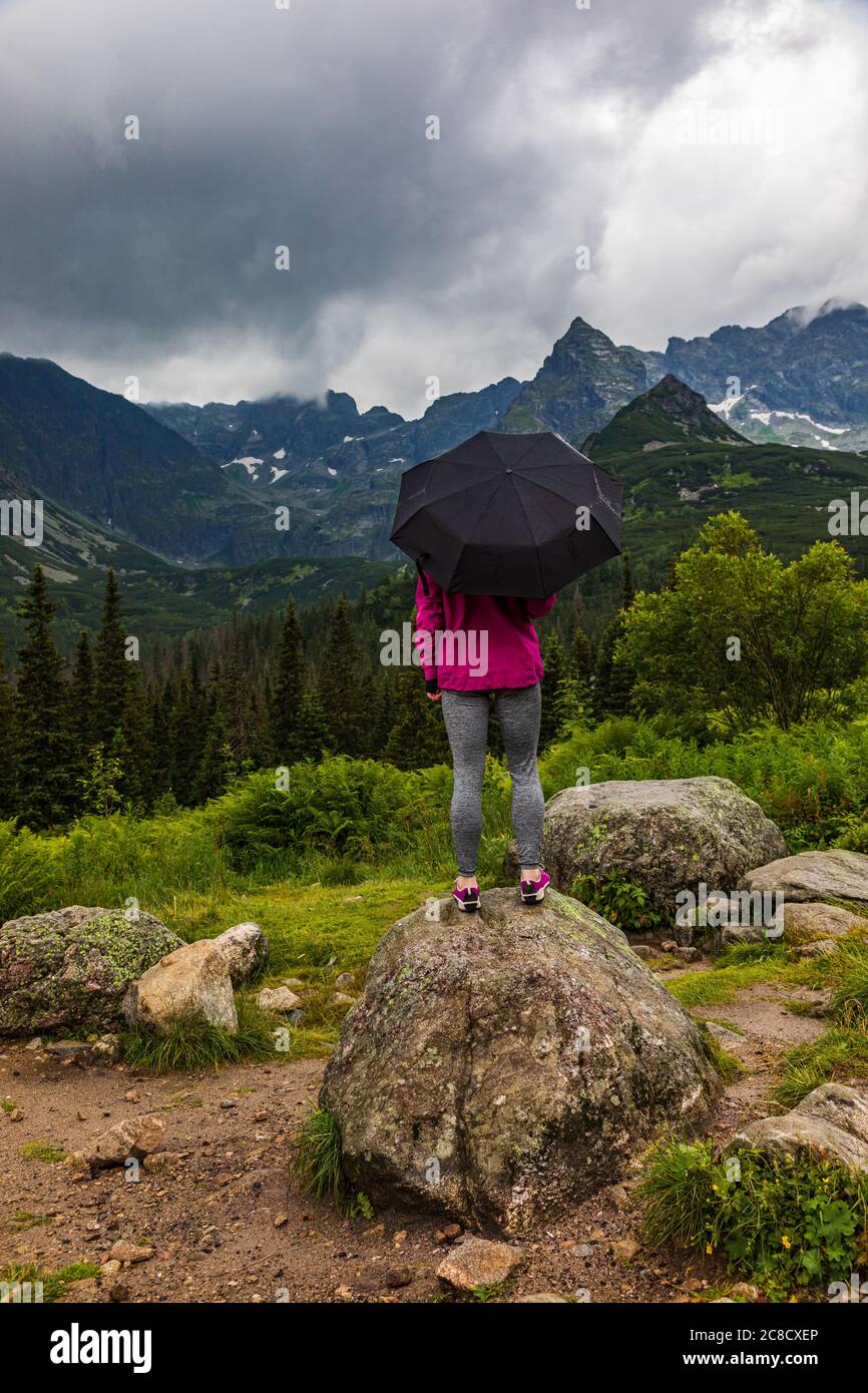 Tourist with the umbrella standing on the stone in the rain in mountain scenery Stock Photo