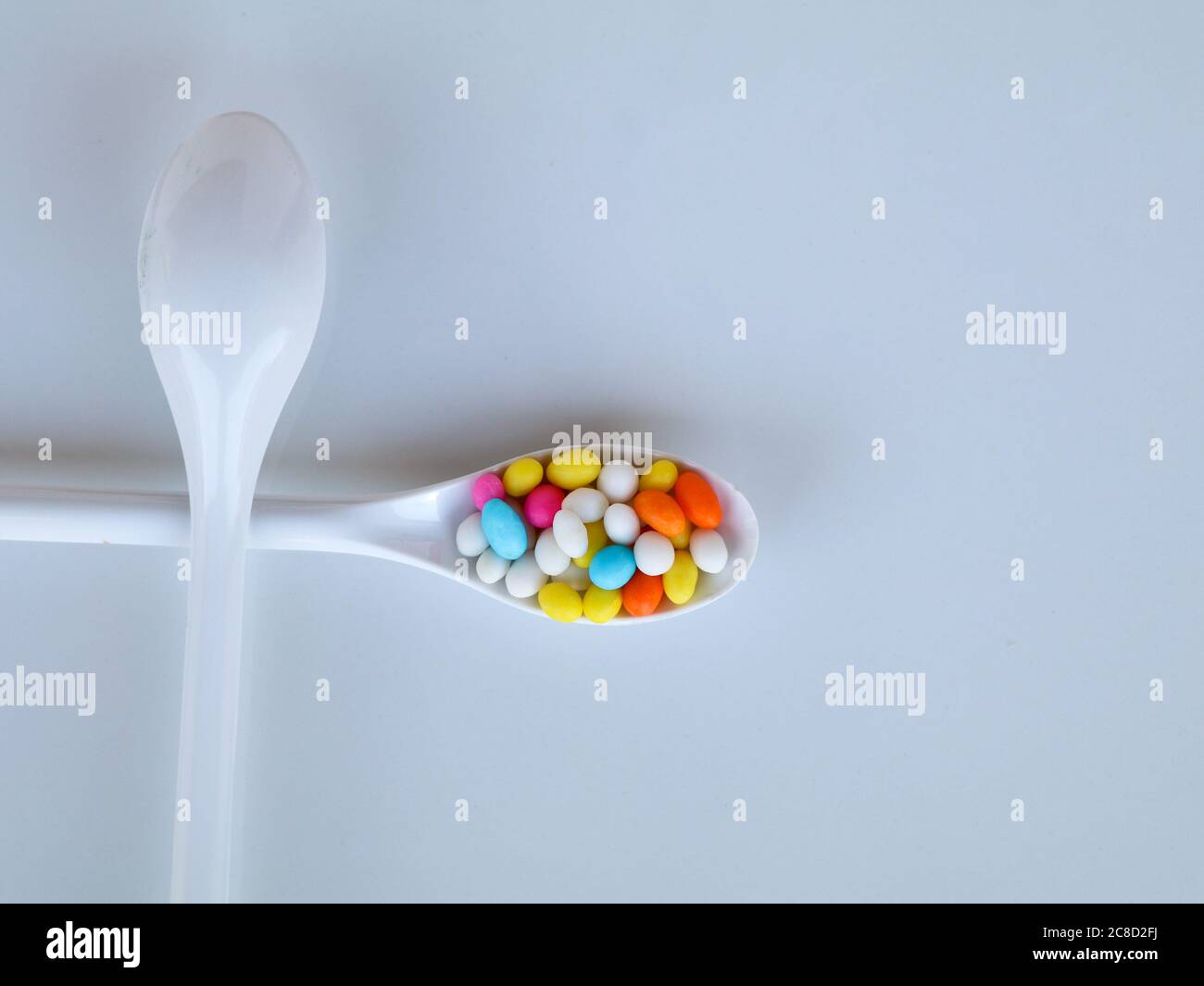 Multi colored sweet fennel sugar candy in white spoons against white