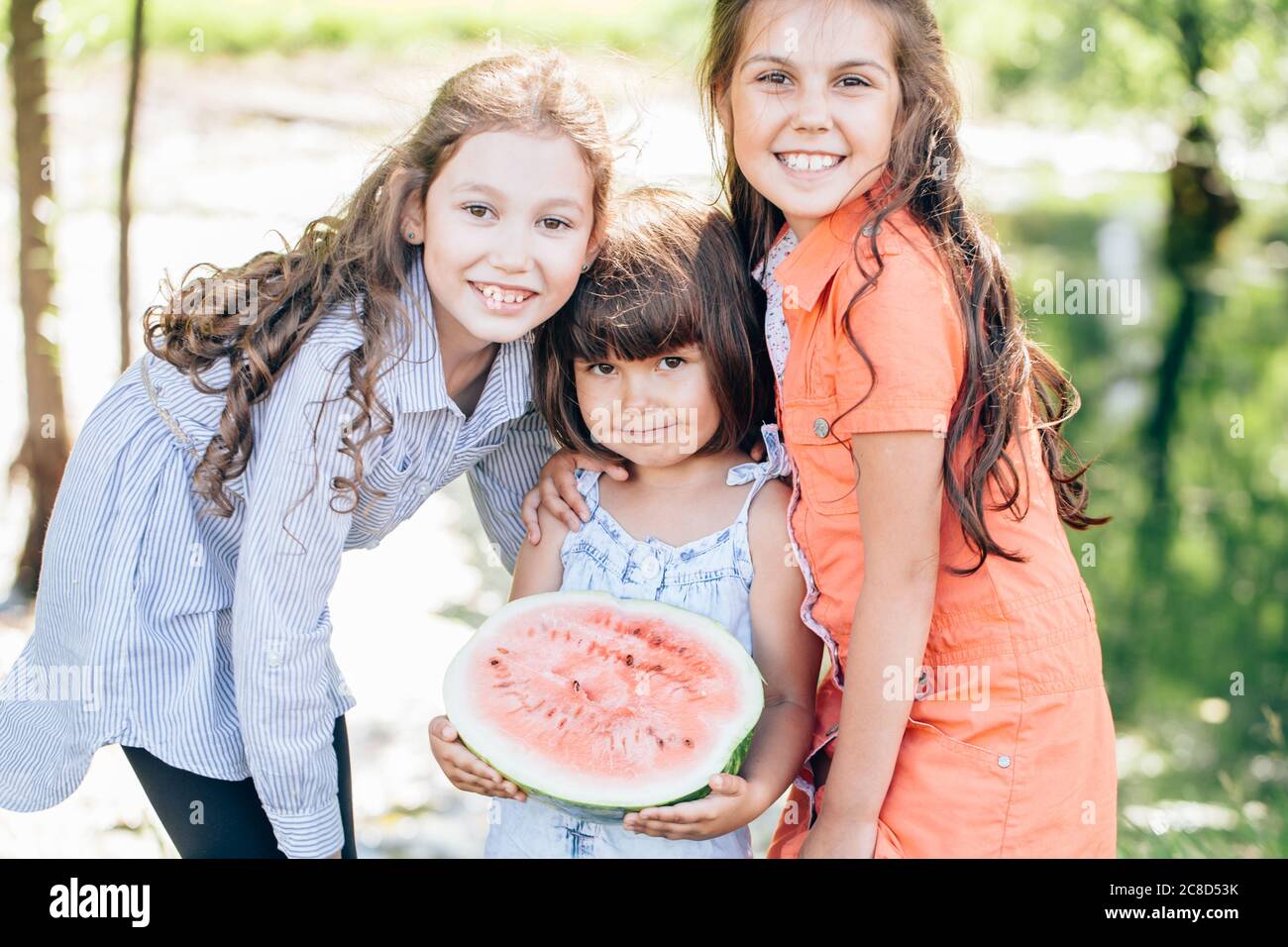 Three young cute funny girls eating watermelon and making funny faces over park outdoor Stock Photo