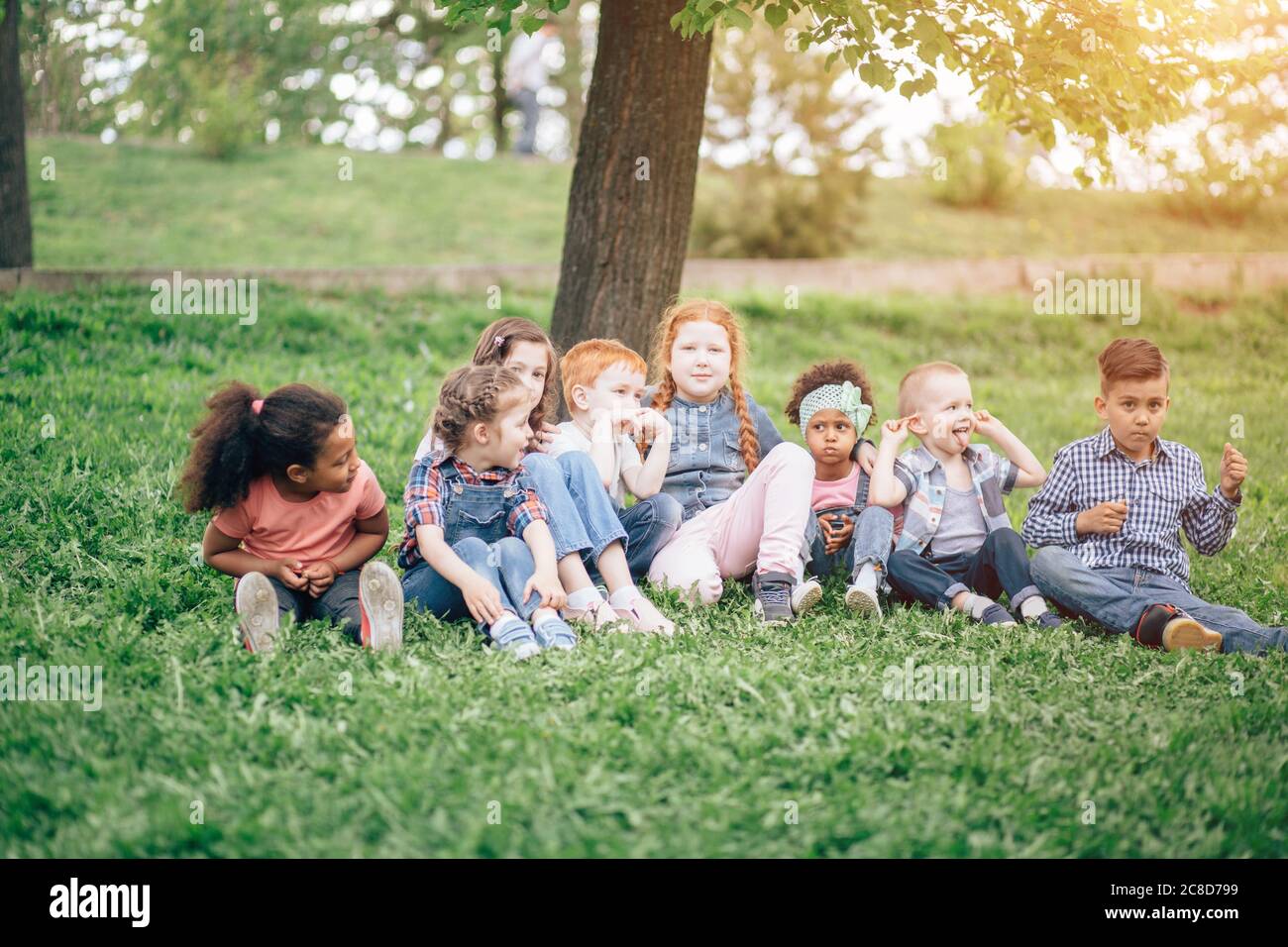 children sitting together on grass in park. concept of childhood, friendship and multicultural communication. Stock Photo